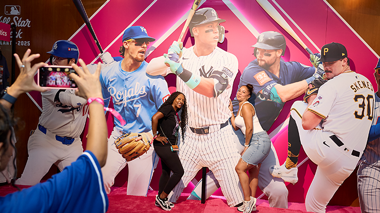 Two friends posing for a picture in front of a large collage of MLB players.