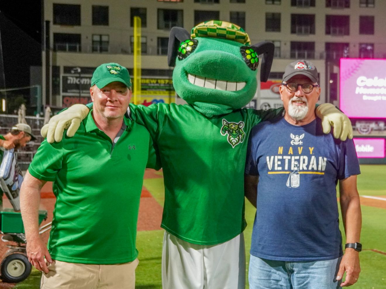 Bob Arnold, a U.S. Navy veteran, stands with a baseball mascot at a baseball field.
