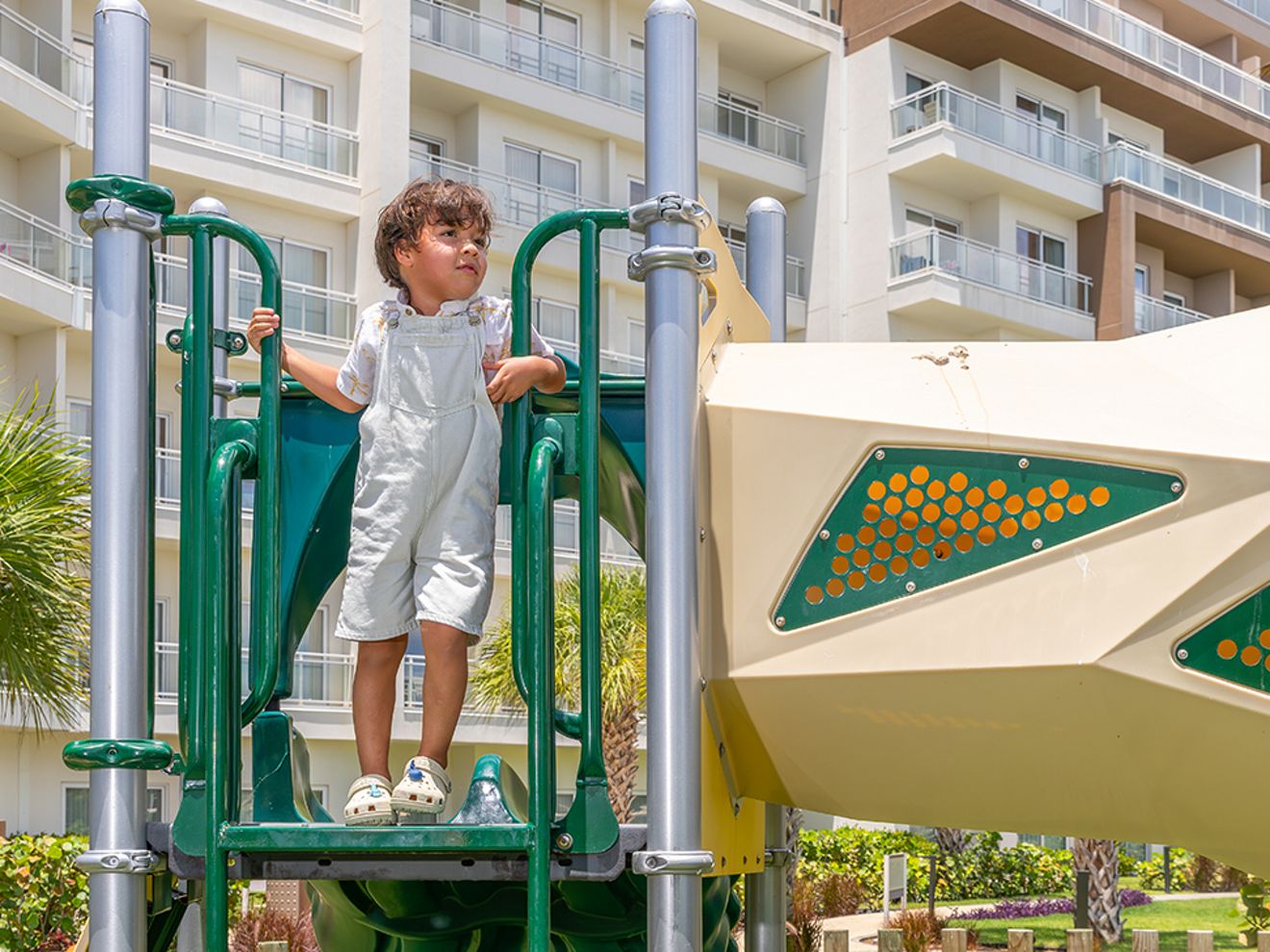 A child stands on a playground structure outside a hotel.
