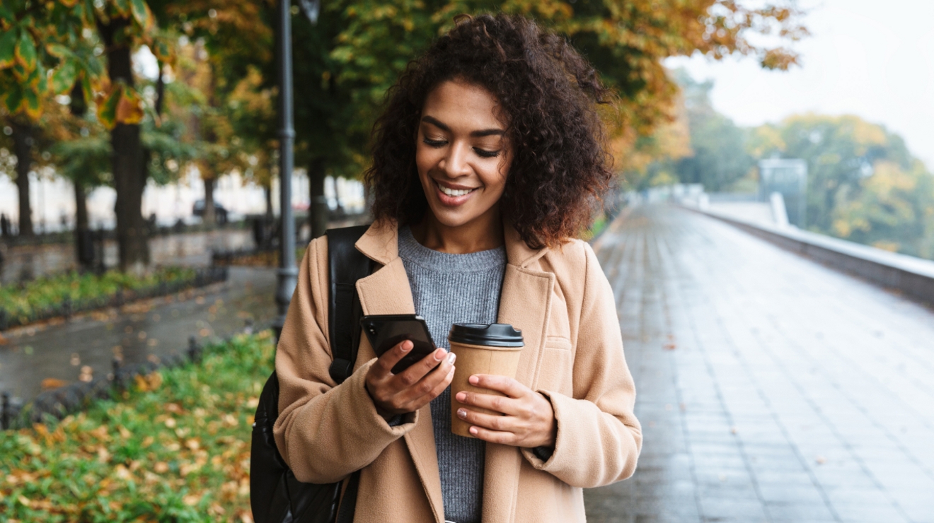 Woman smiling at her phone and holding a coffee.