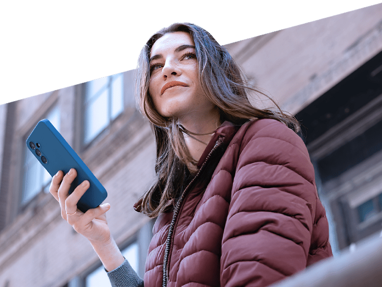 A woman holds her smartphone and looks into the distance.