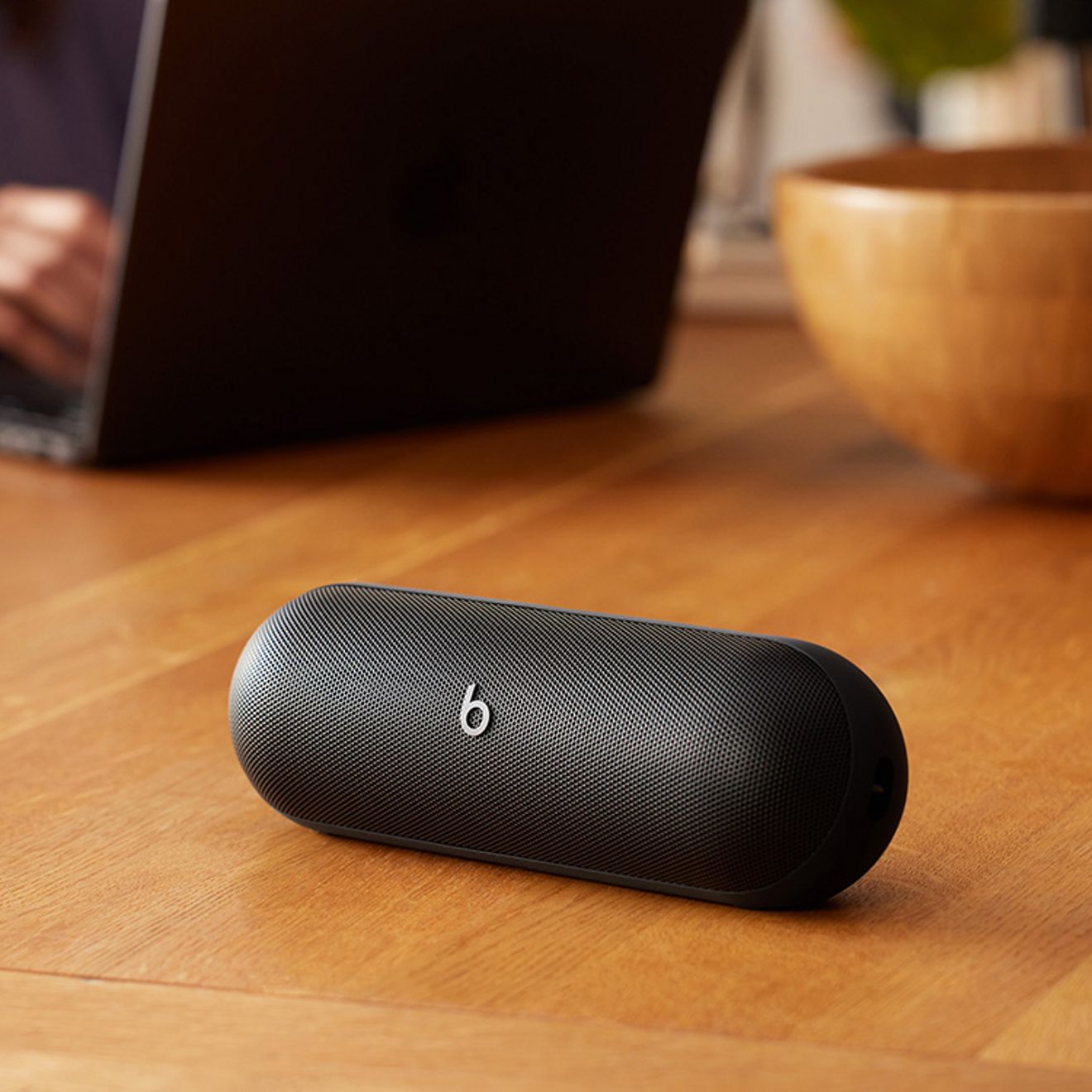 Black beats pill sits in foreground while someone works on laptop. 