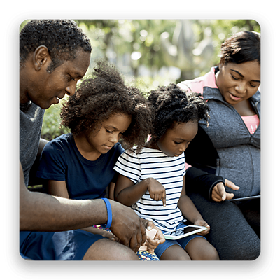 A family of four look at mobile device screens while sitting in a park.