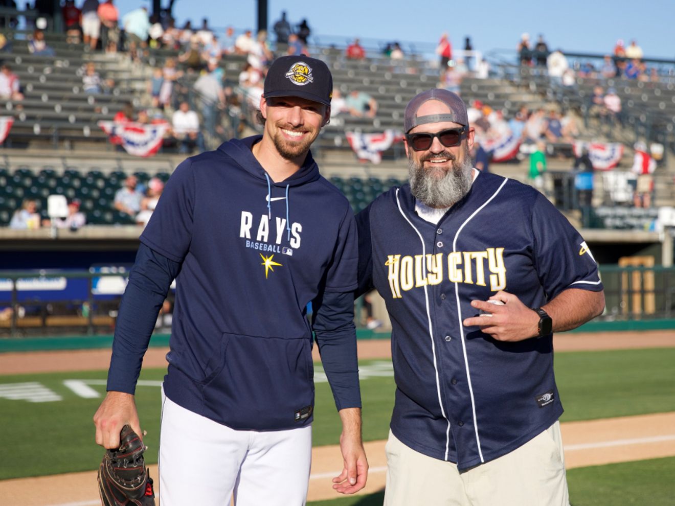 Jon Wellington, a U.S. Navy veteran, stands on a baseball field with a baseball player.