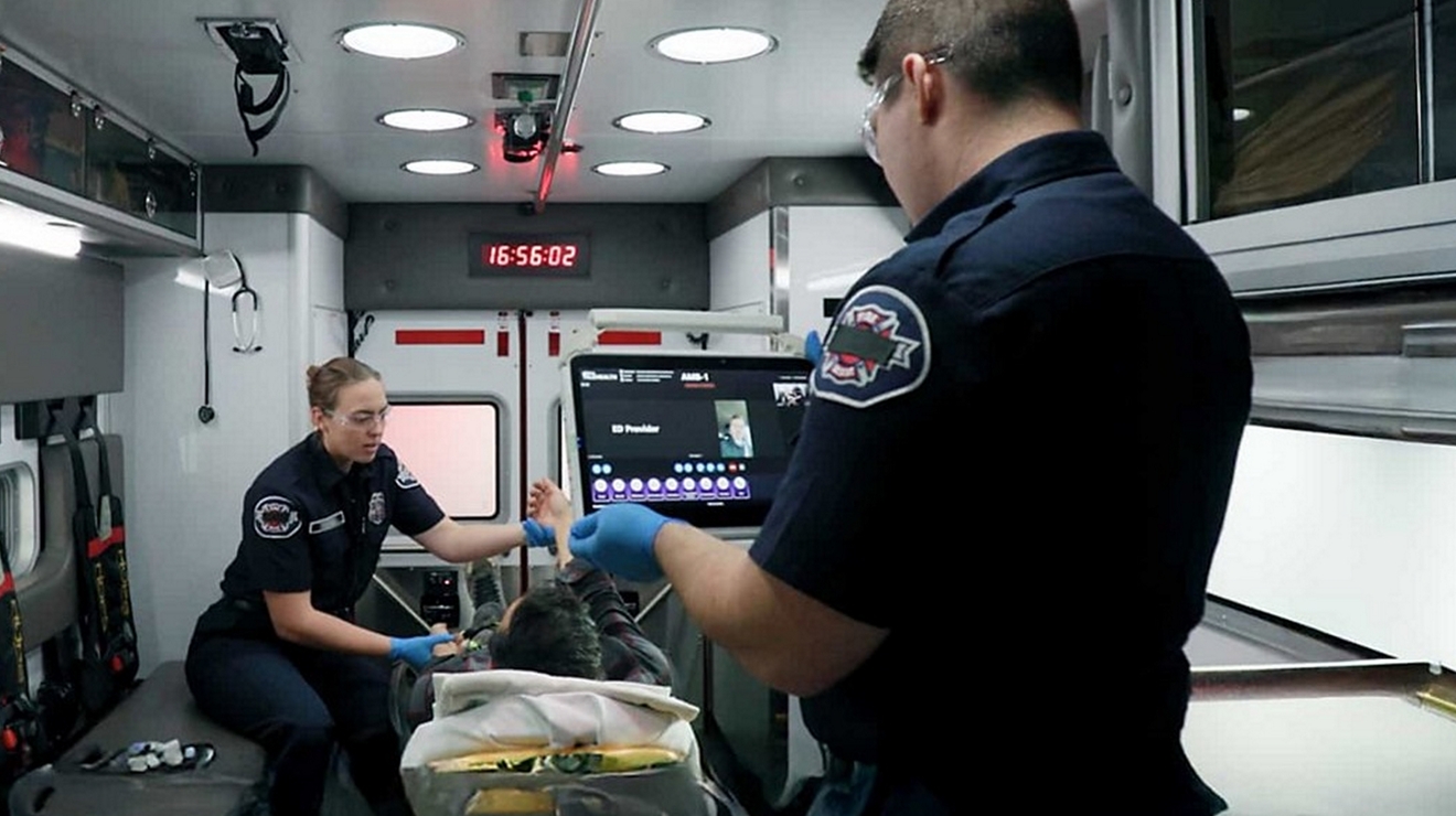Paramedics provide emergency care inside an ambulance while using real‑time digital tools to monitor and coordinate patient treatment.