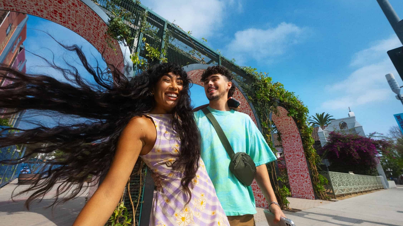 Couple laughing while one of them holds a phone in his hand, with an outdoor setting and a blue sky in the background.