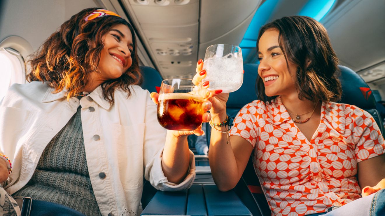 Two Delta passengers tapping their drinks together in a toast. 