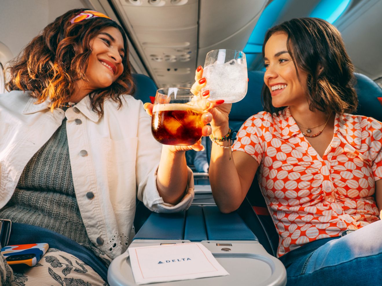 Two Delta passengers tapping their drinks together in a toast. 