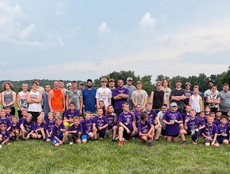 The Eastern High School football team poses for a photo with a group of children wearing purple shirts.