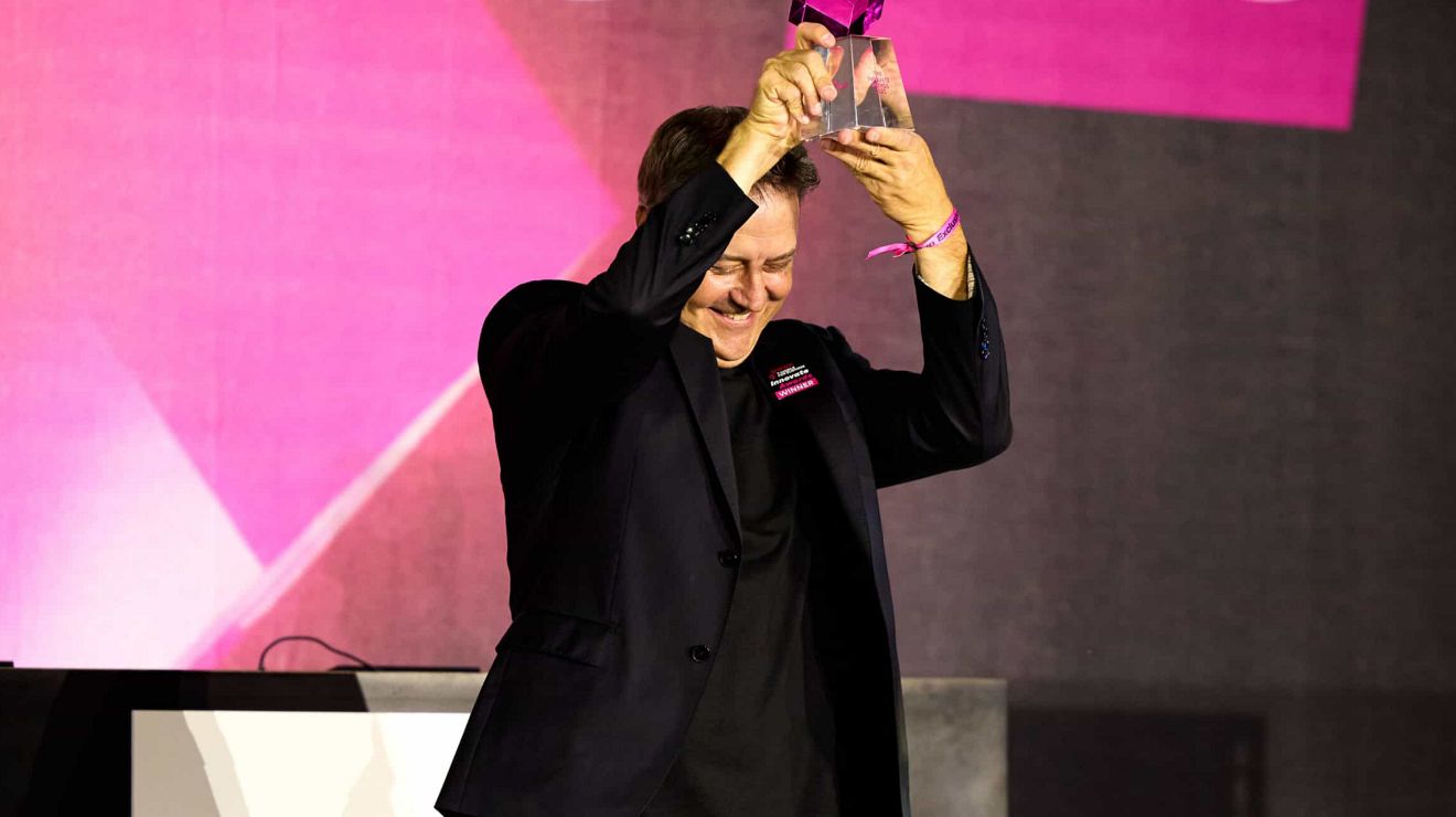 A previous Innovate Awards winner wearing a black blazer holds a trophy in the air.