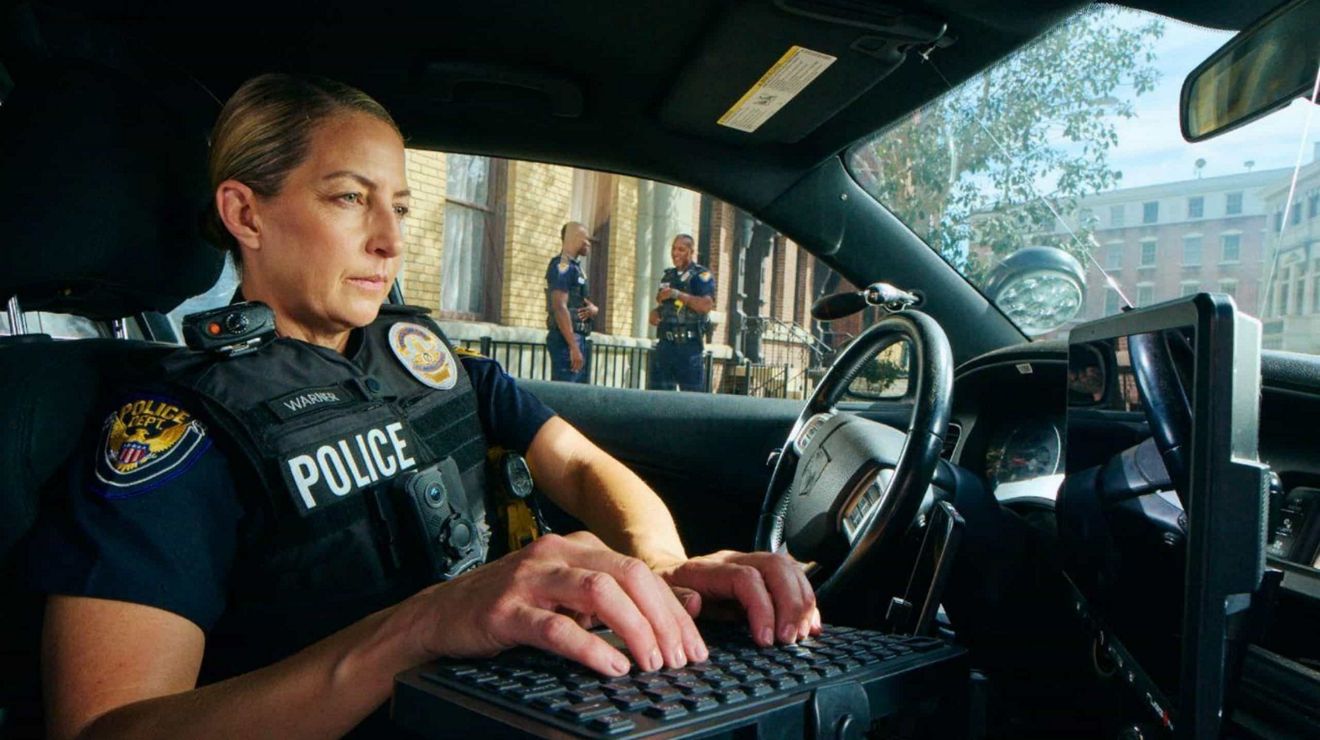 A police officer in a car uses a monitor and keyboard to transmit mission-critical updates