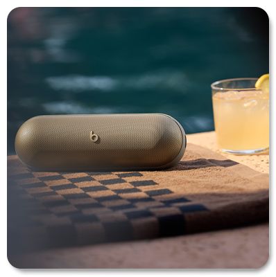 Champagne gold Beats Pill sitting on a towel by the pool with a drink behind it.
