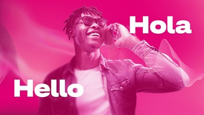 A man in a white t-shirt, denim jacket, and sunglasses smiles widely as he holds a phone to his ear. “Hello” and “Hola” appear around him.