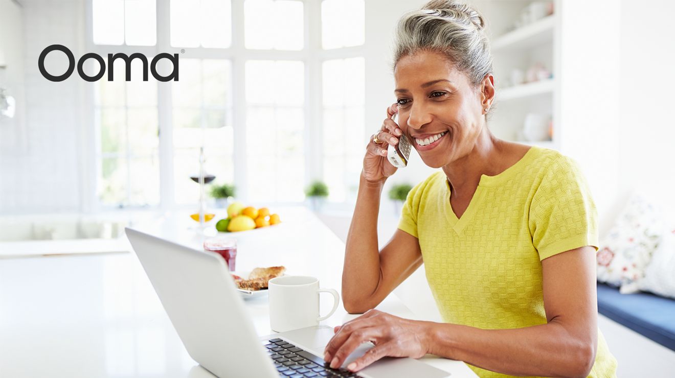 Ooma. Smiling woman talking on a landline phone while reclined in a chair.