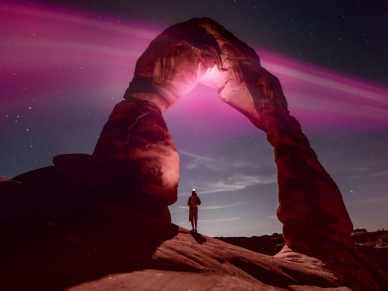 Person standing under natural stone arch with Magenta rays above