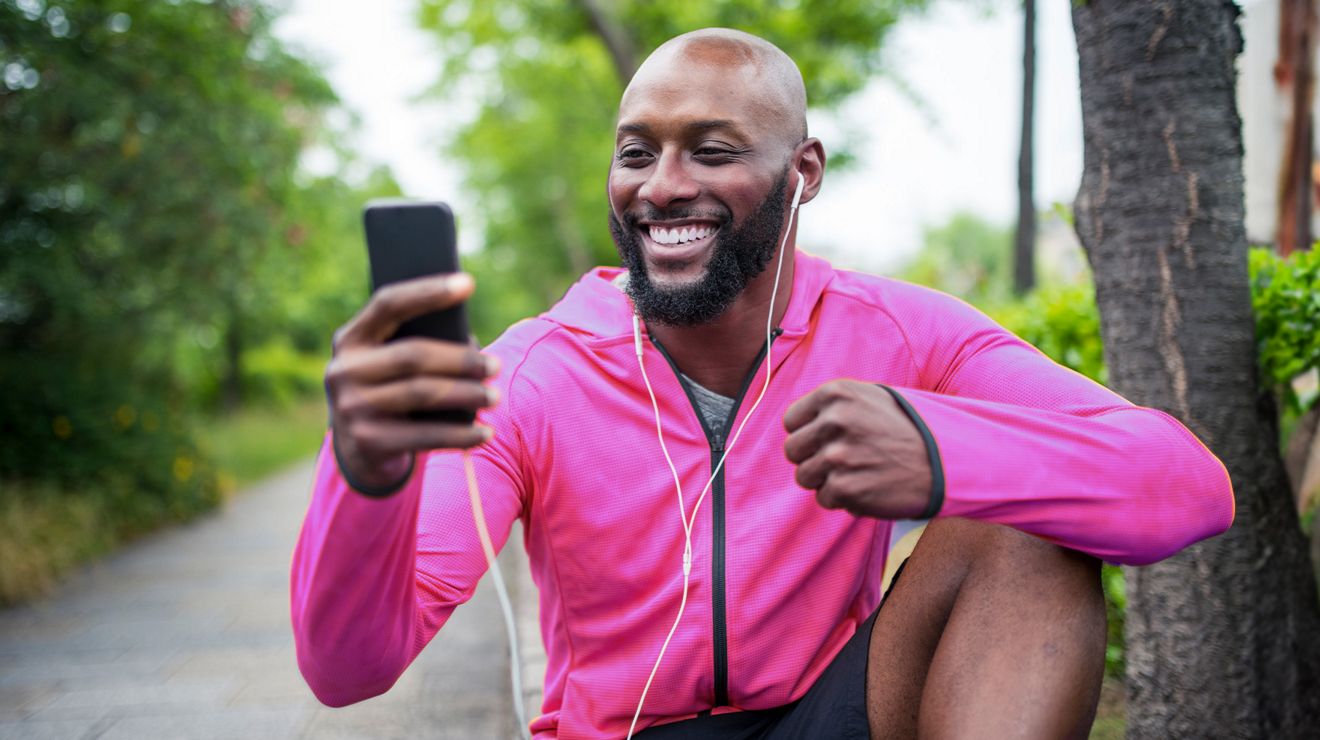 Man in a pink jacket smiling while looking at his phone outdoors.
