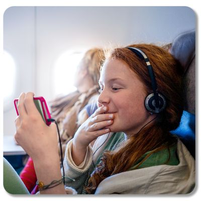 A girl wearing headphones smiles at her phone while aboard a plane.