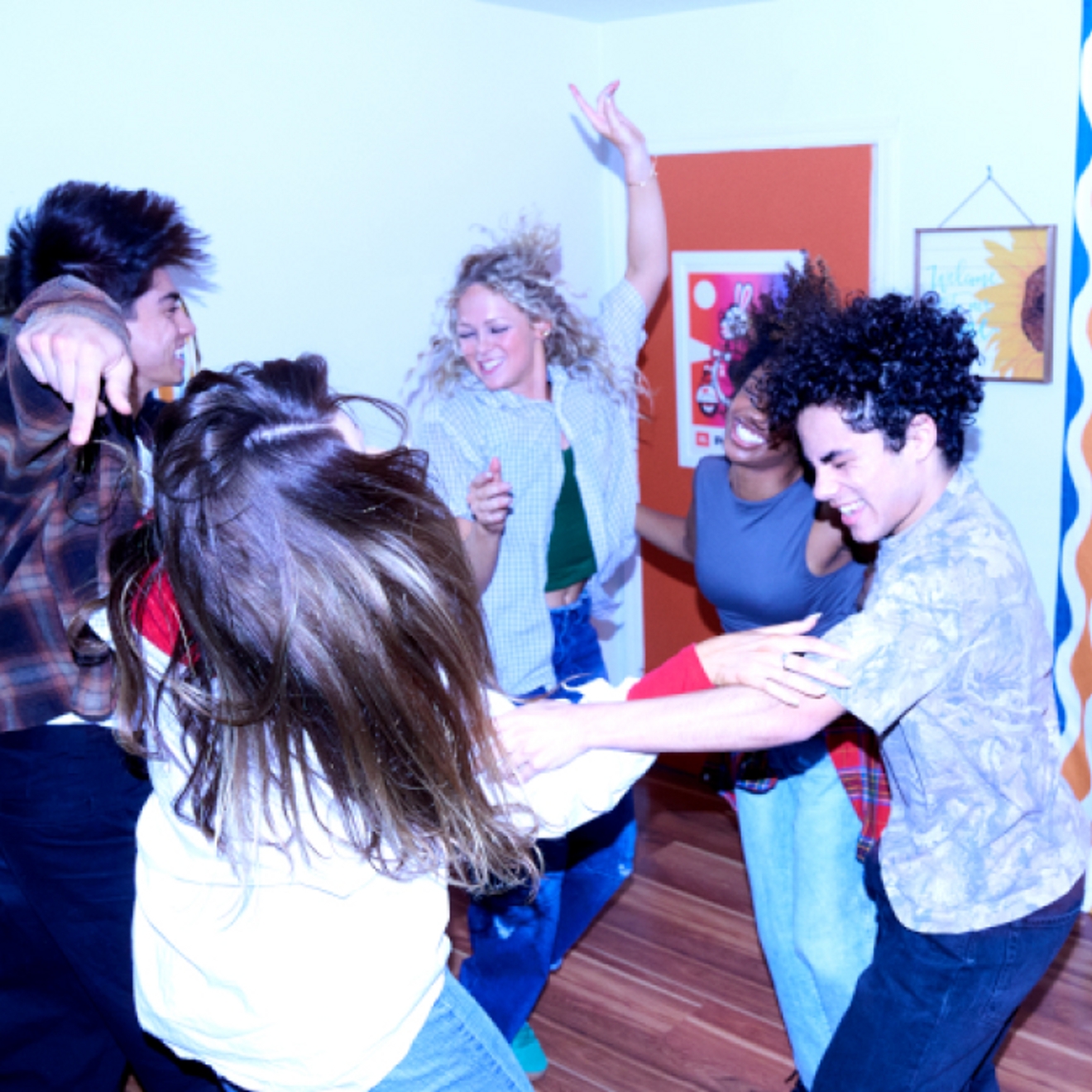 Five friends dancing in a circle in an apartment.