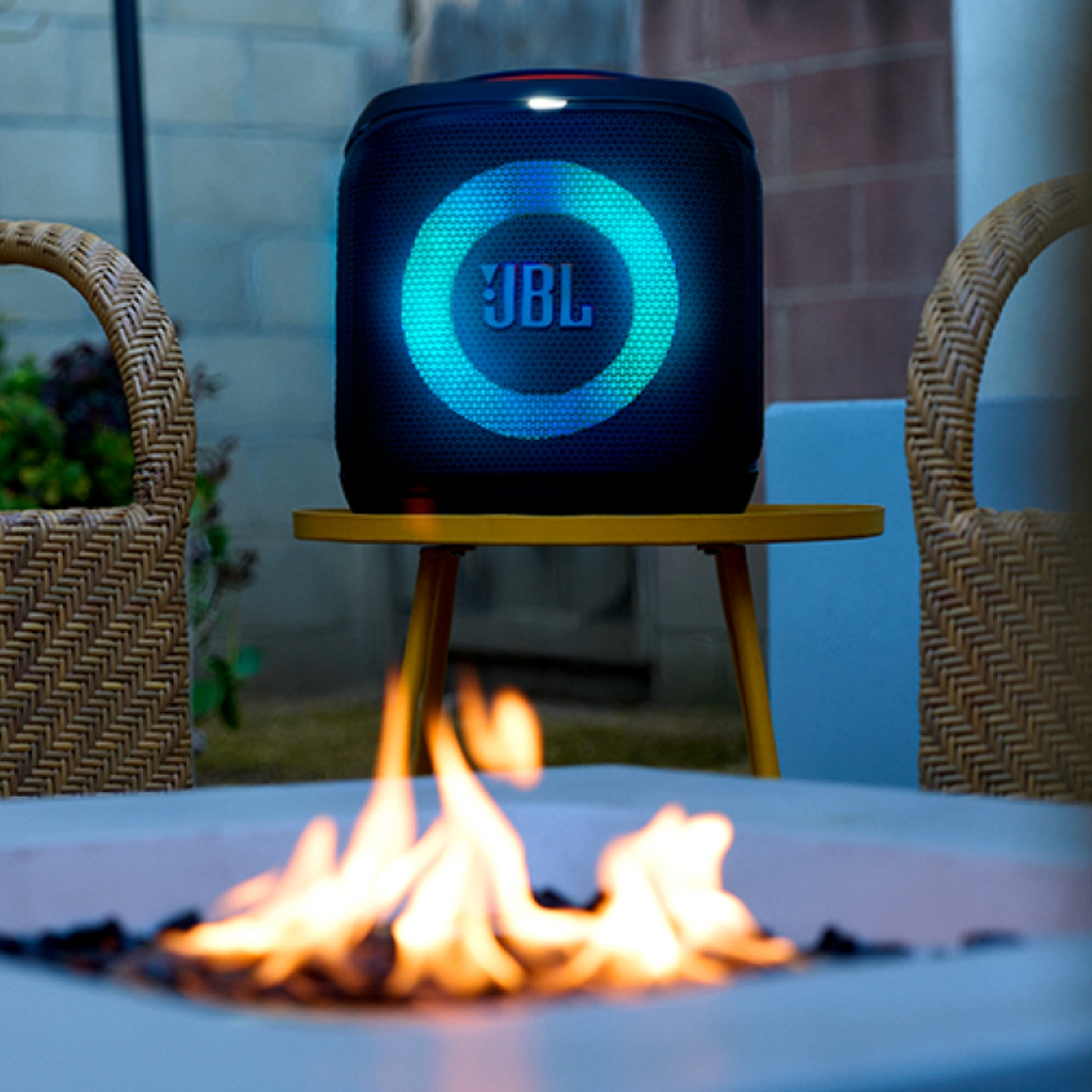 A close-up image of a JBL speaker glowing blue while next to a firepit.