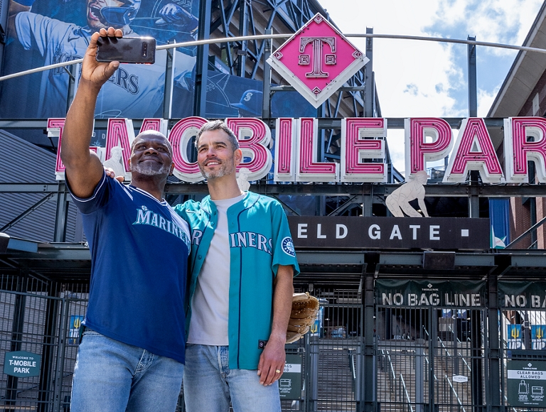 Two friends pose for a selfie outside the entrance to a baseball field.