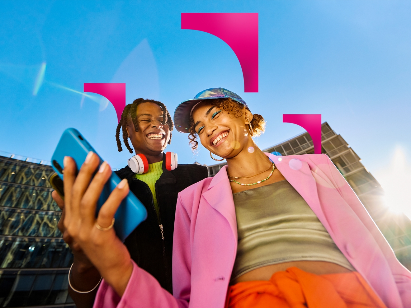 Two smiling people with smartphones in hand outside on a sunny day. 