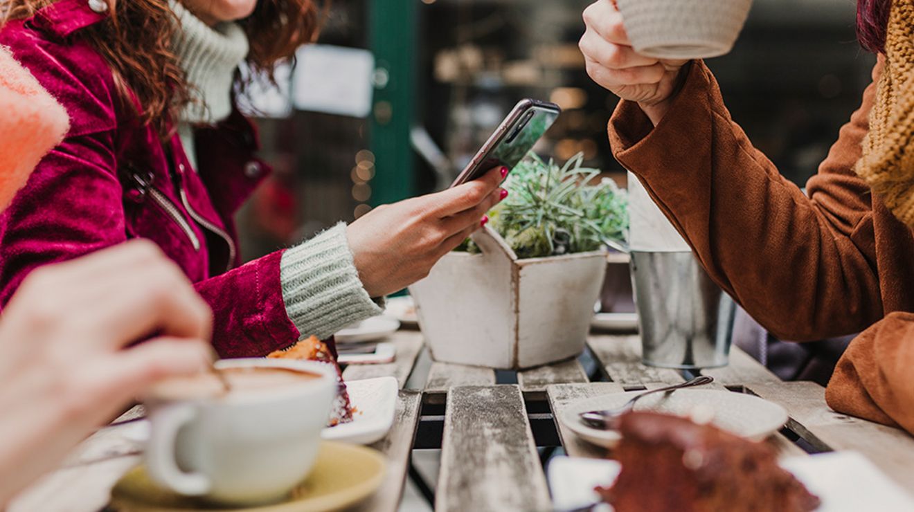 Woman holding phone as she shares coffee and dessert with friends.
