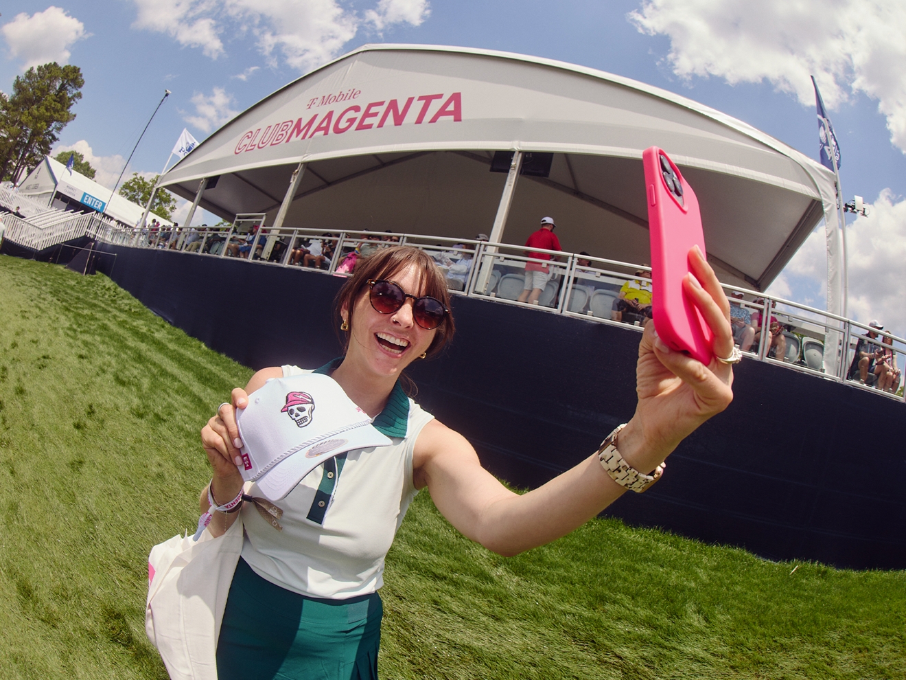 Golf fan taking a selfie with a T-Mobile and Devereux Golf co-branded hat in front of Club Magenta. 