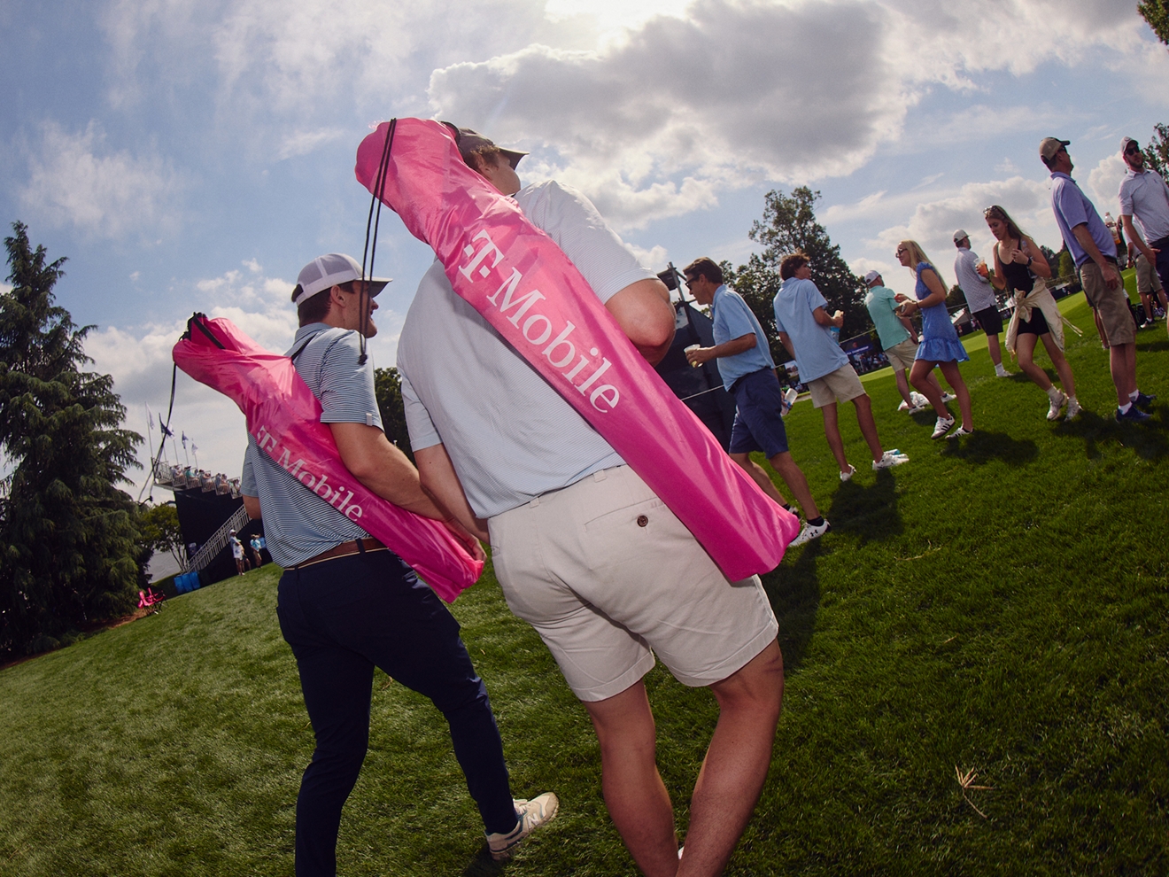 Two people carrying T-Mobile branded lawn chairs across a golf course. 
