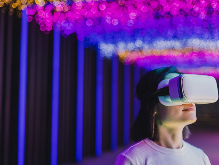 A person wears a virtual reality headset in room lit with soft, multi-colored lights. 