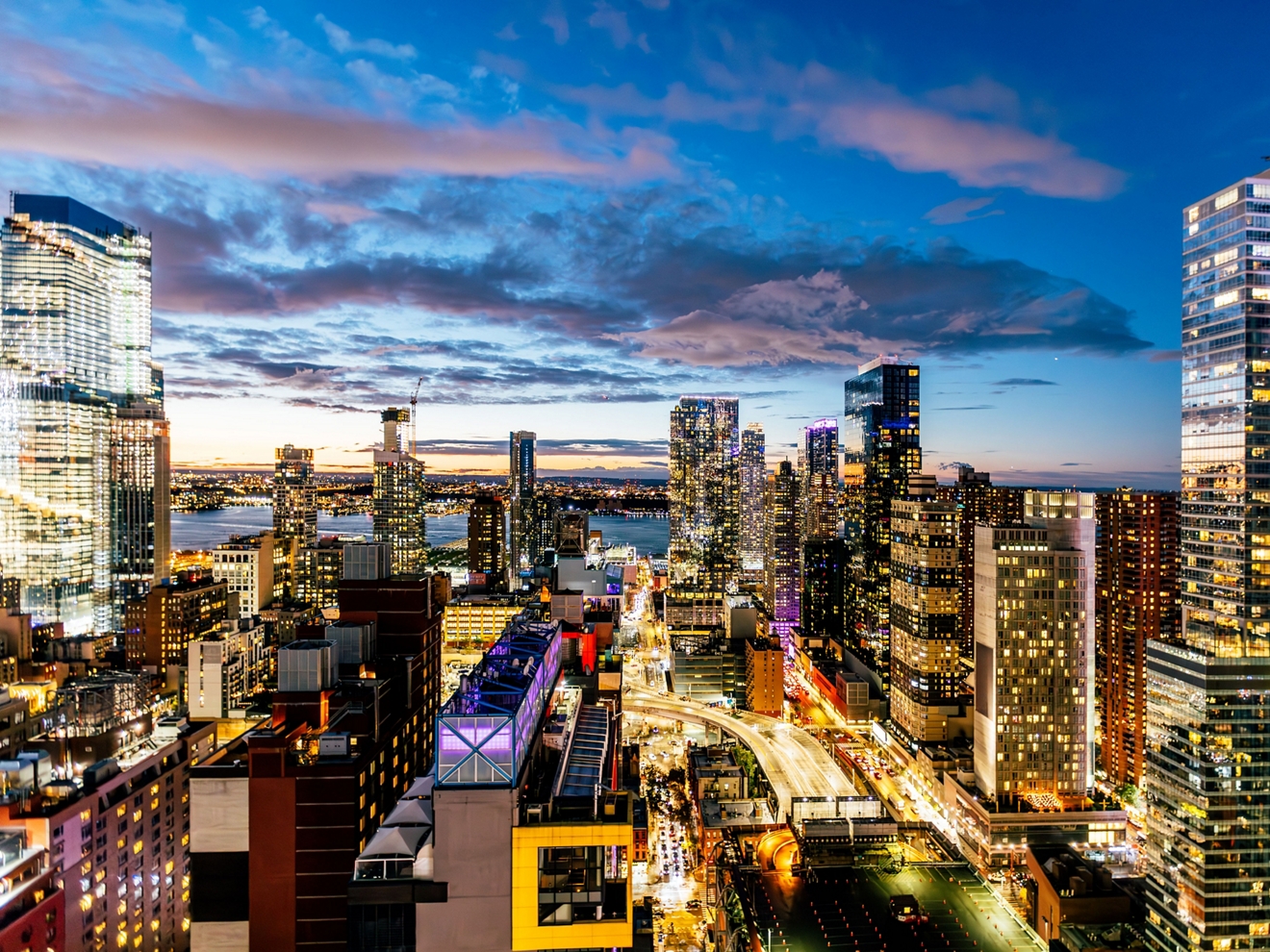 A cityscape at dusk, with busy streets glowing with headlights and skyscrapers lit up against the sky.