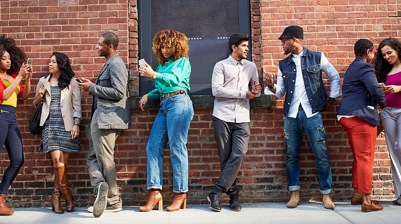Group of people using their phones while waiting in line outside a restaurant or concert venue.