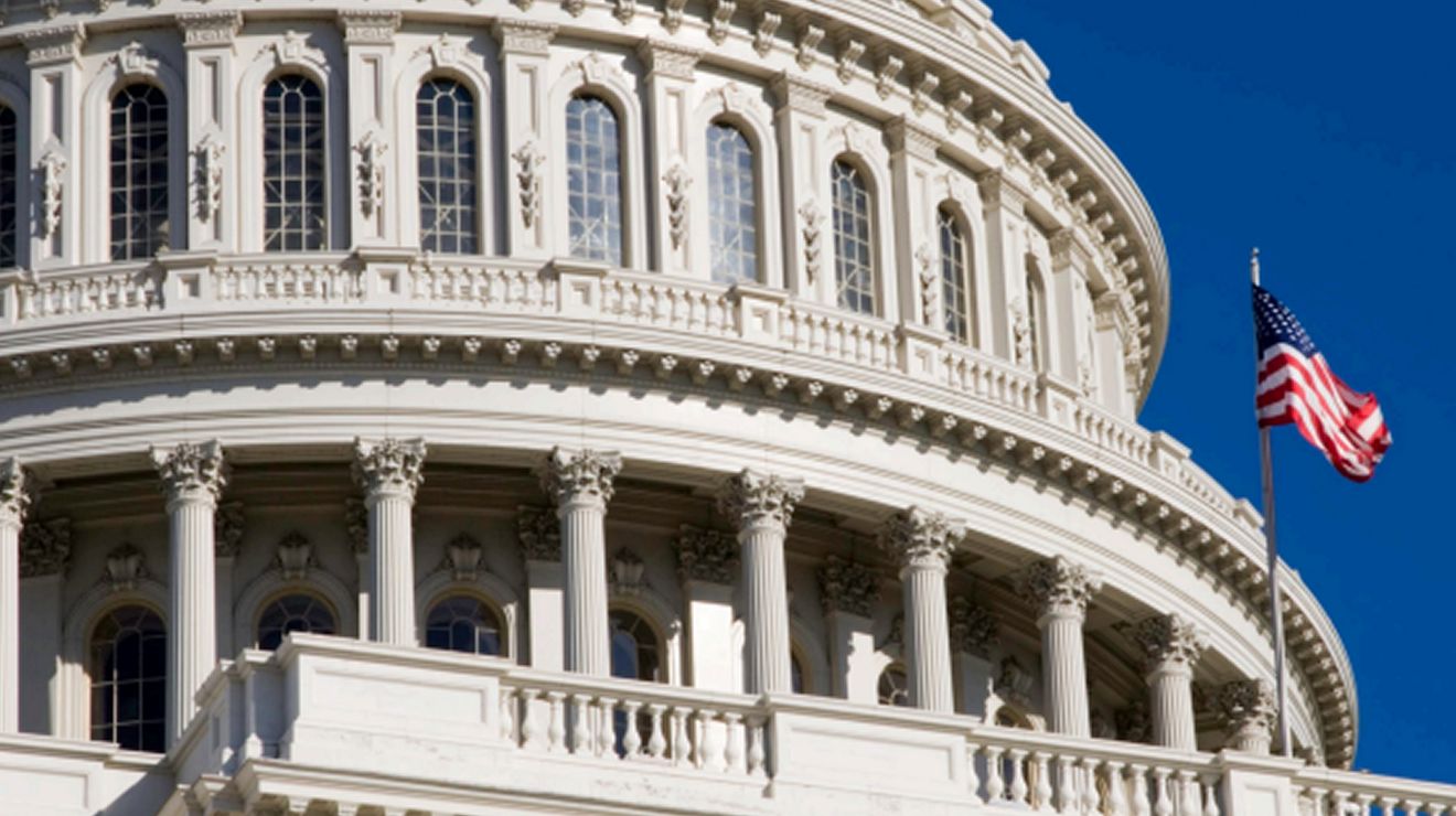 Close up of the U.S. Capitol dome and American flag against a blue sky.