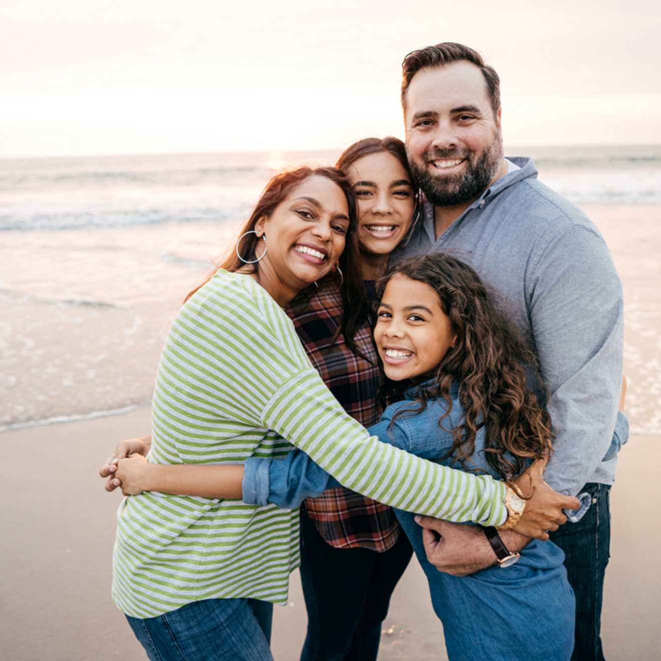 Family of four posing for a photo on a beach.