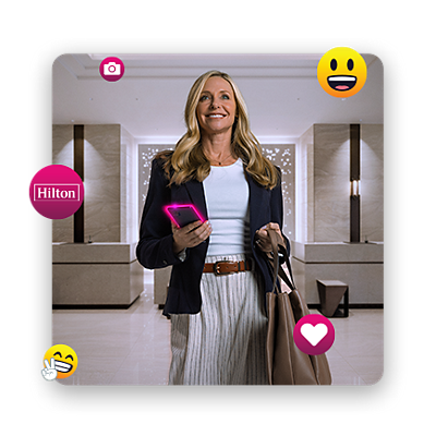 A woman, surrounded by happy emojis, stands in the lobby of a Hilton hotel with a back in her hand.
