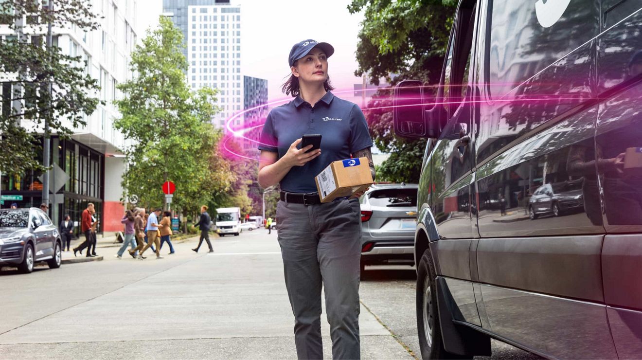 A woman in a delivery-style uniform walks along a city sidewalk holding a package and a phone, while magenta beams surround her as she is next to a van.