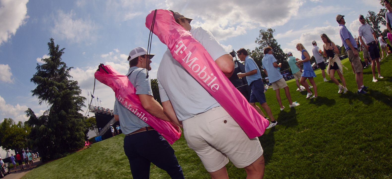 Two T-Mobile members carrying lawn chairs onto the golf course. 