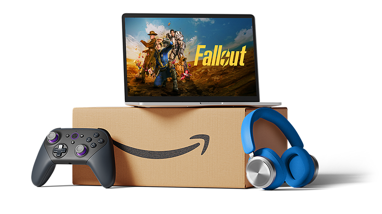 A laptop with the Amazon Prime show Fallout on screen, stacked on top of a box, with a game controller and headphones next to the box.