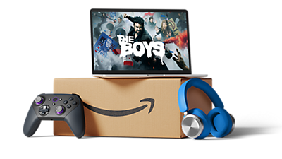 A laptop with the Amazon Prime show The Boys on screen, stacked on top of a box, with a game controller and headphones next to the box.