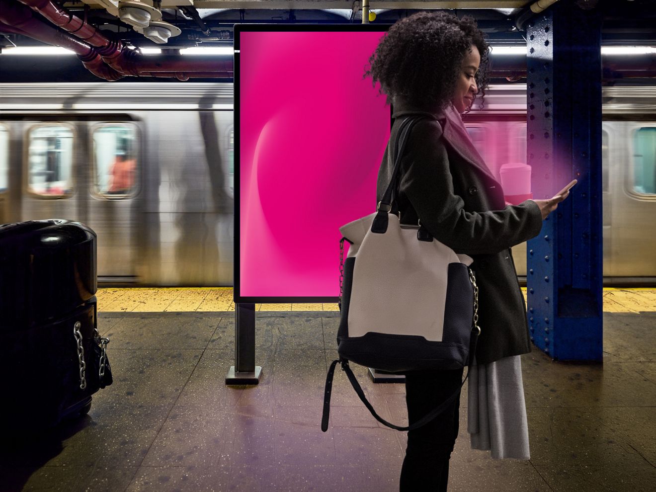 Woman using her phone near a digital out-of-home sign with a mass transit train passing behind her.