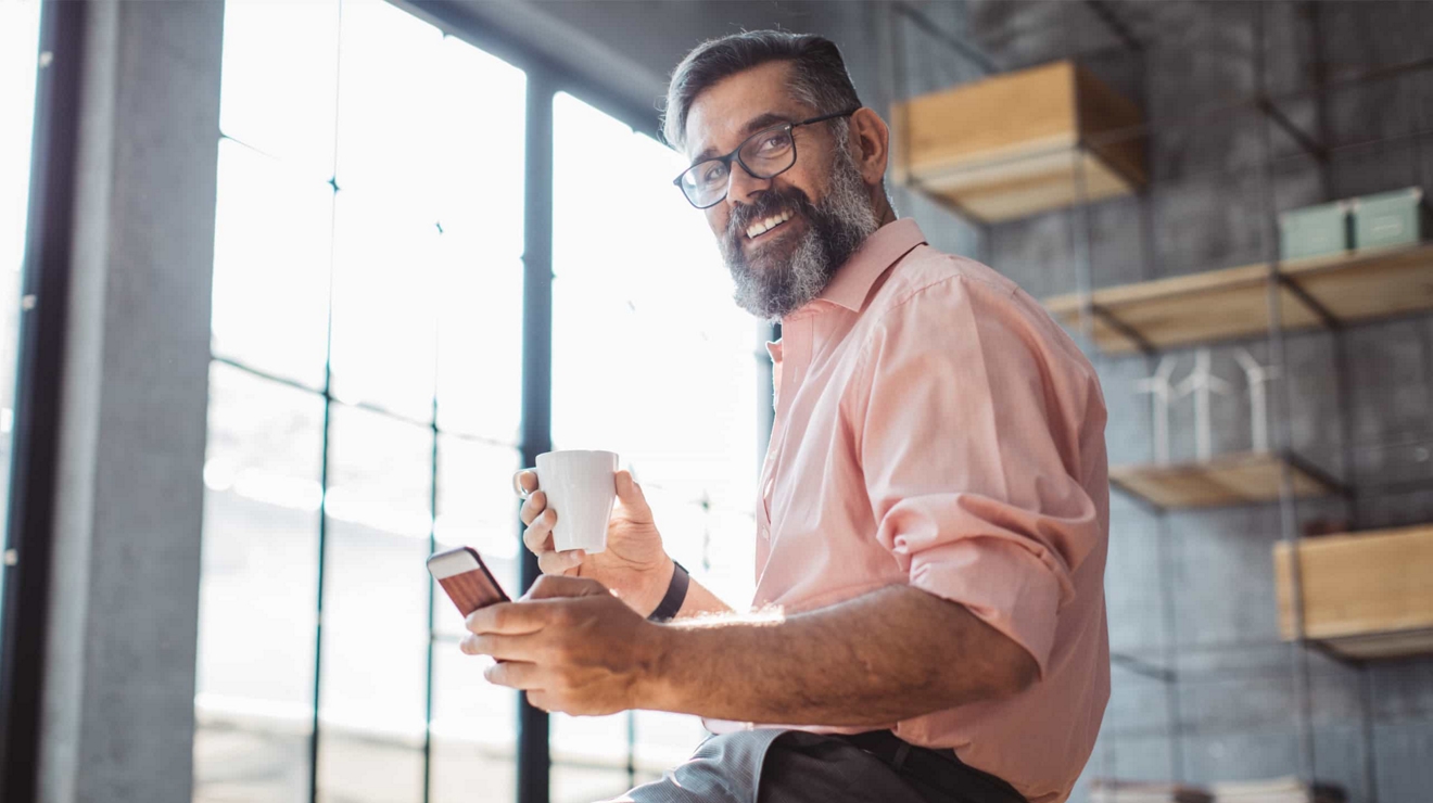 A business professional holding a cup of coffee smiles as they check their 5G-connected smartphone.