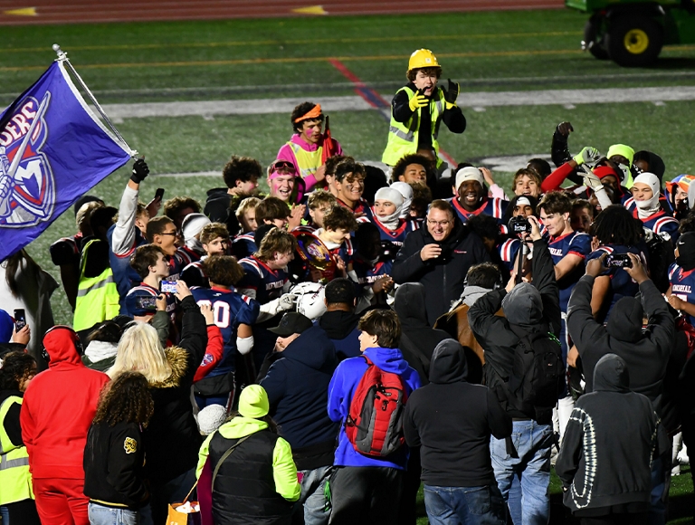 A group of Manchester football players and other students huddle on the field after a game.