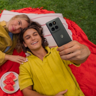 Two friends laying down on a picnic cloth with food, taking a selfie with a moto edge.