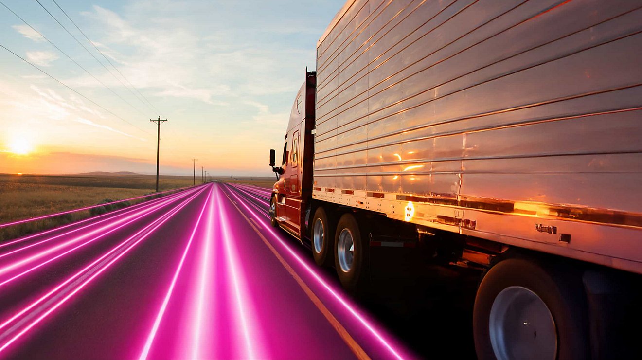 A semi-truck rolls along a lonely, magenta-colored highway at dawn.