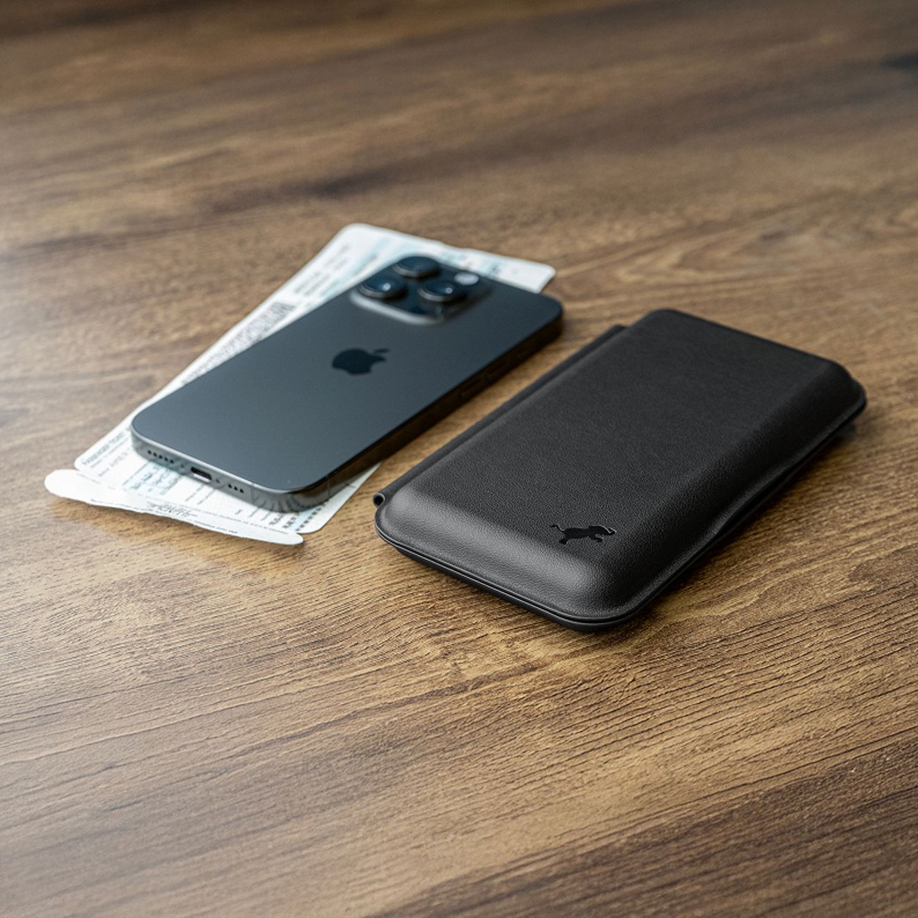 A black Nimble Fold 3-in-1 wireless charger folded flat beside an iPhone and boarding passes on a wooden table.