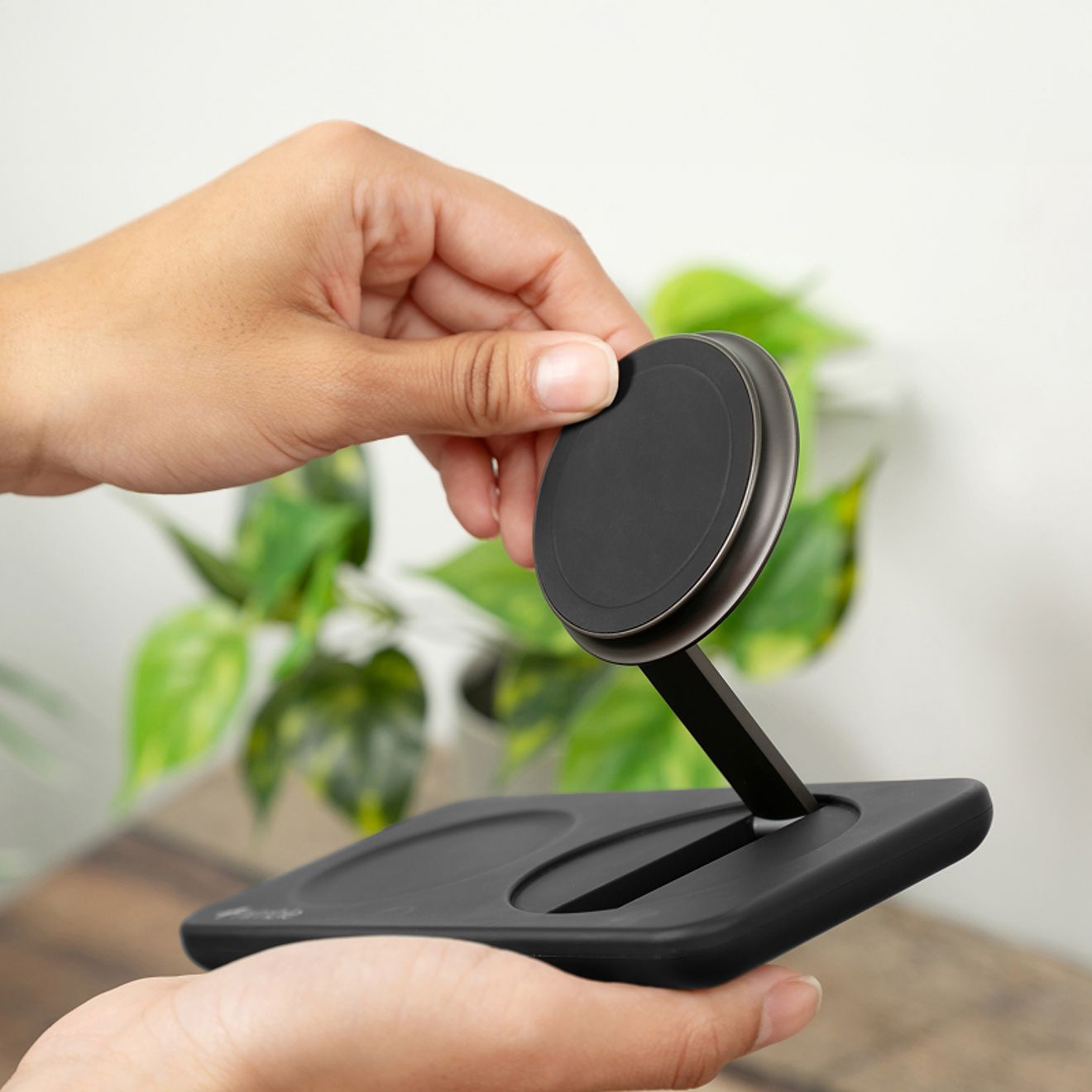 A black Nimble Fold 2-in-1 wireless charging station sits in a person’s hand, with dedicated charging areas for a smartphone and wireless earbuds.