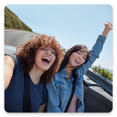 Two women take a selfie in the back of a convertible car.