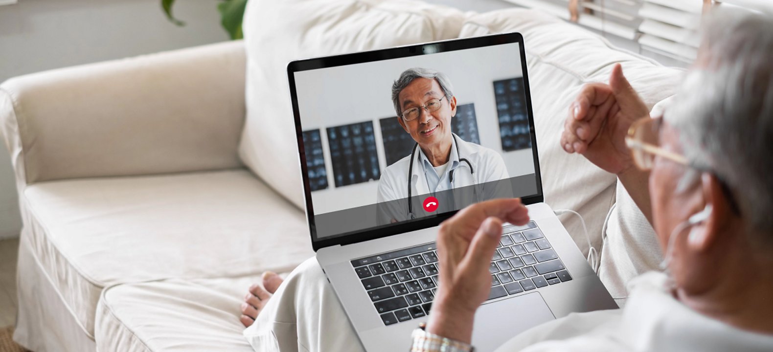 An older man meets with his doctor at a telehealth appointment from a couch in his home.