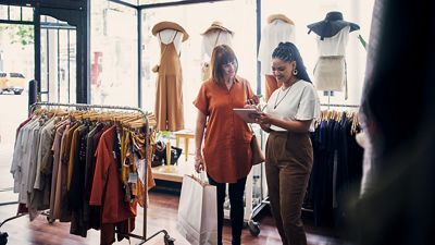 An employee at a boutique clothing store uses a POS-equipped tablet to help a customer make a purchase.