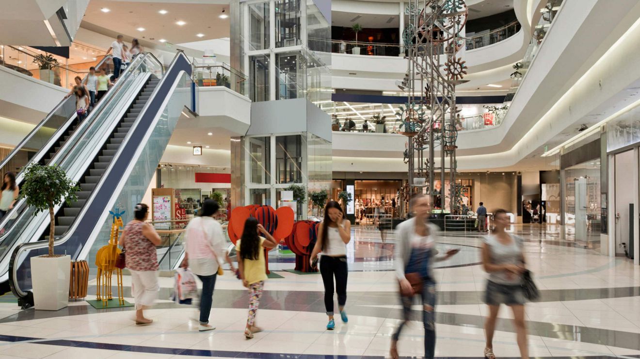 Customers doing their shopping in a busy, multi-story mall with an elevator.