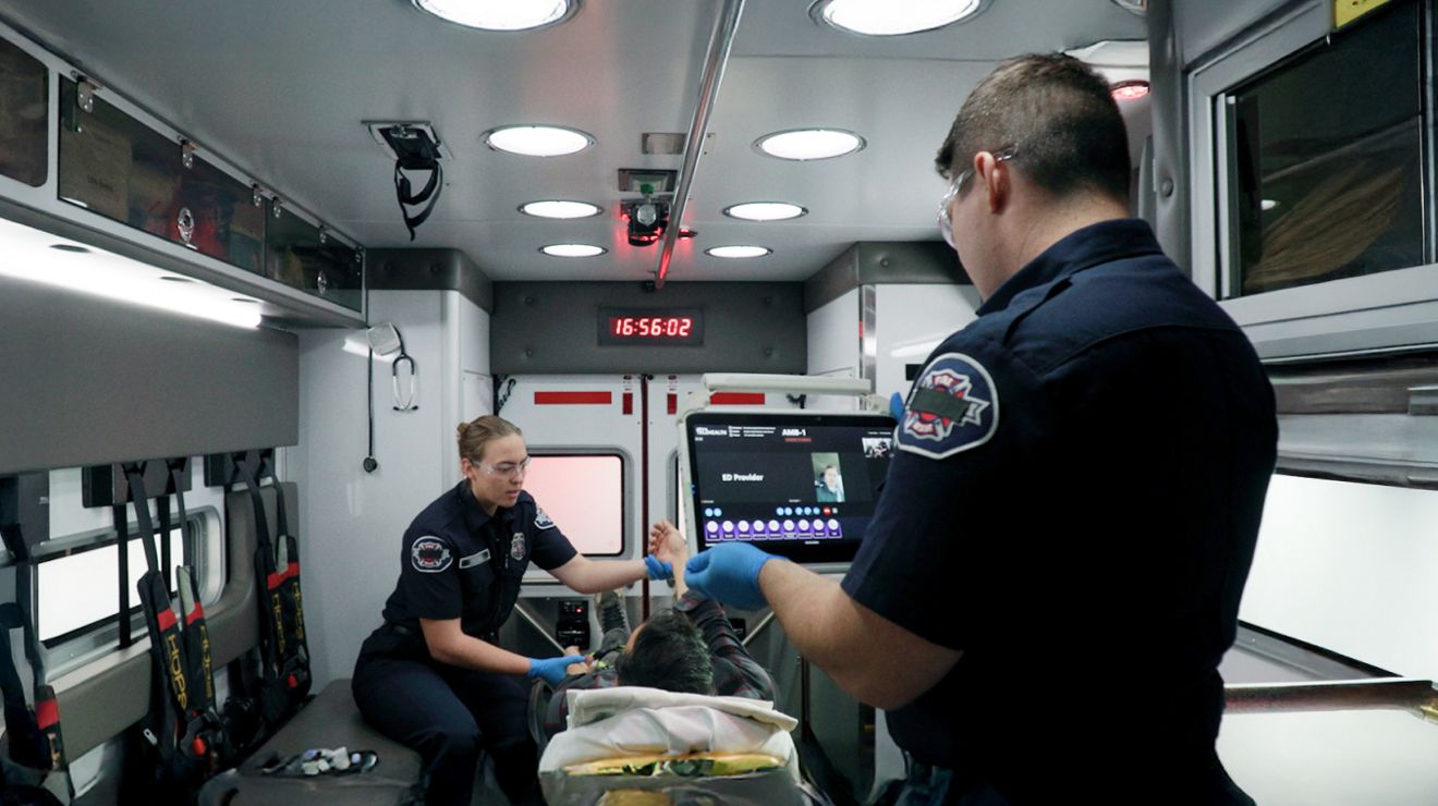 Paramedics provide emergency care inside an ambulance while using real‑time digital tools to monitor and coordinate patient treatment.